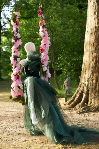 Suknia uszyta przez Natalię Ślizowską, prezentowana na manekinie siedzącym na huśtawce ozdobionej kwiatami